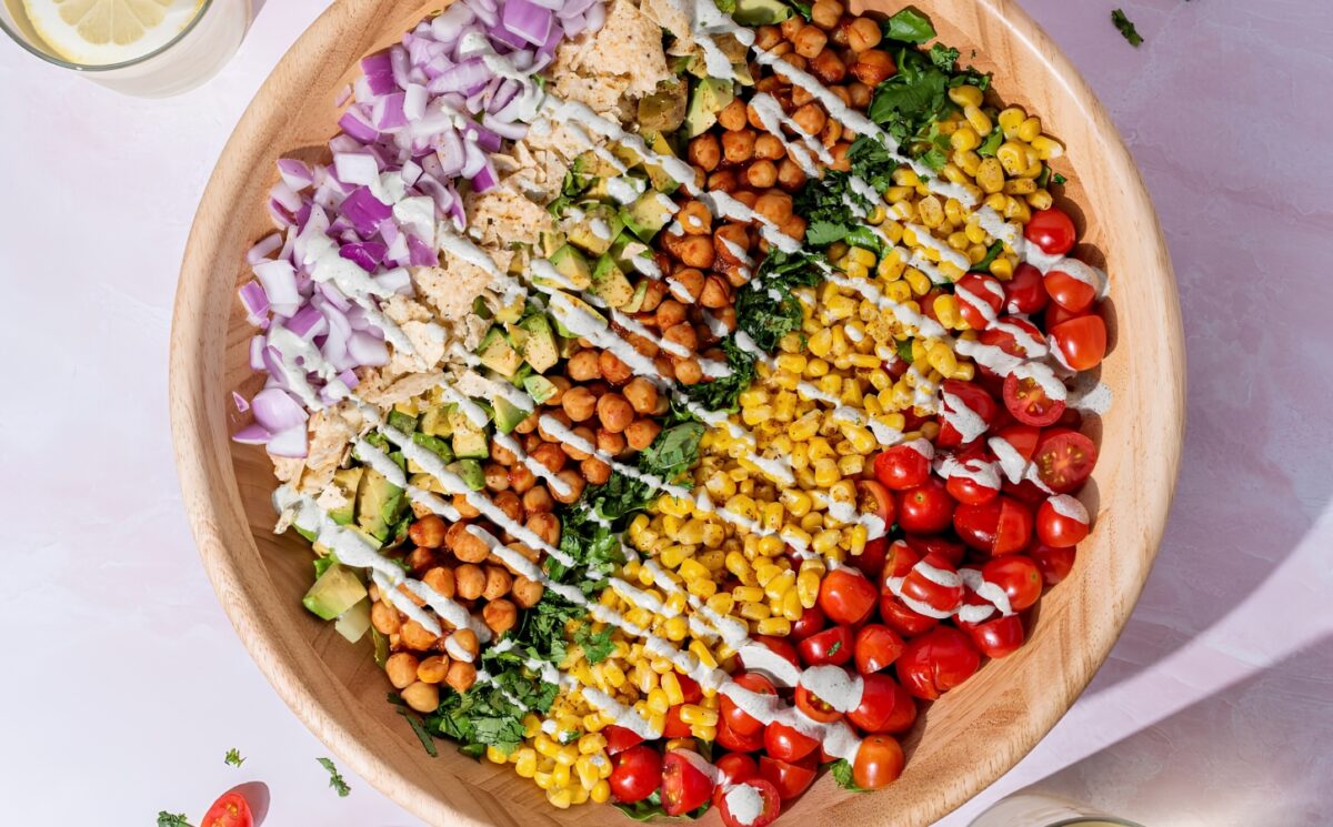 Photo of a beautifully assembled chickpea barbecue salad with tomatoes, corn, chickpeas, lettuce, corn chips, hemp seed dressing and a variety of other vegetables for a gluten-free lunch idea