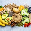 A view from above of a large number of foods containing a lot of dietary fiber. The composition includes blueberries, oranges, avocados, whole grain bread, potatoes, oats, corn, beans, vegetables, broccoli, mixed nuts, bananas, among others.
