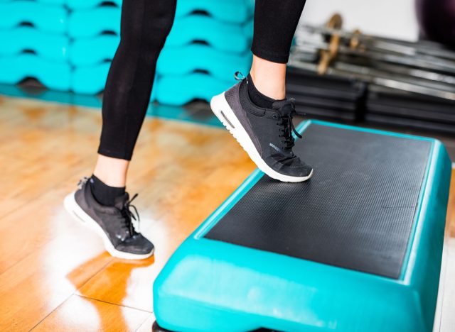 Fit brunette girl in black shoes, black leggings, blue and yellow sports clothes and shirt in the gym working on fitness.