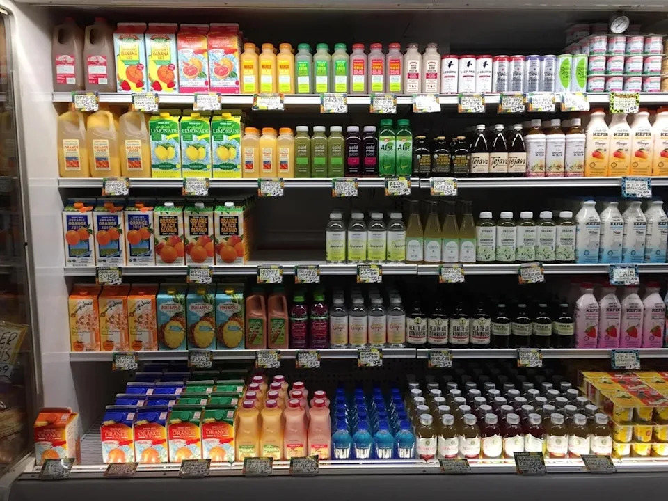 Grocery store shelves are lined with bottles of a variety of juices and beverages labeled with different flavors and brands.