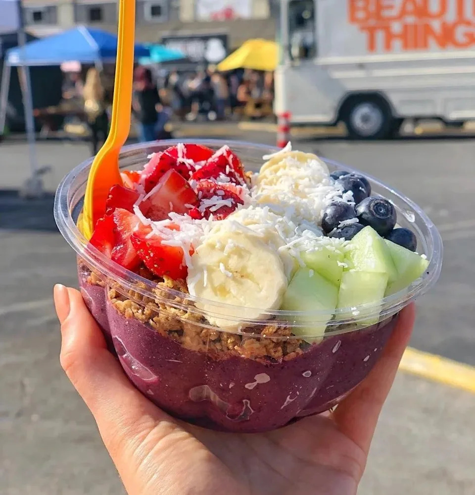 Smoothie bowl with sliced ​​strawberries, bananas, blueberries and melon in hand. Granola and coconut flakes add texture