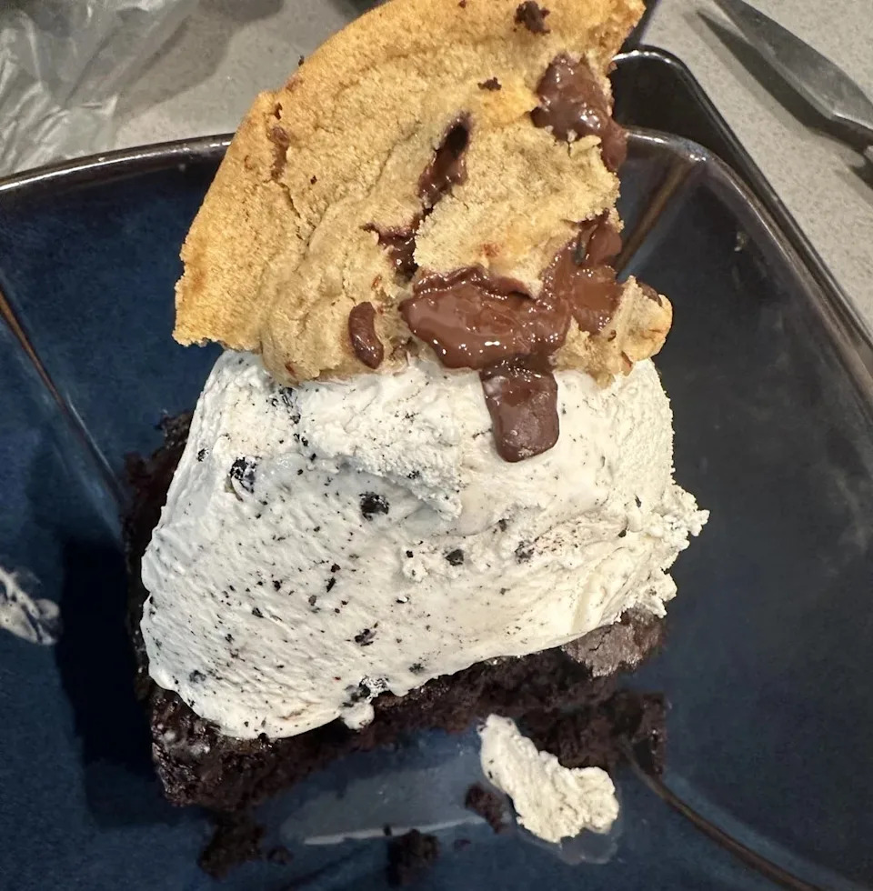 A decadent dessert made with chocolate cake topped with cookies and cream ice cream and topped with chocolate chip cookies.