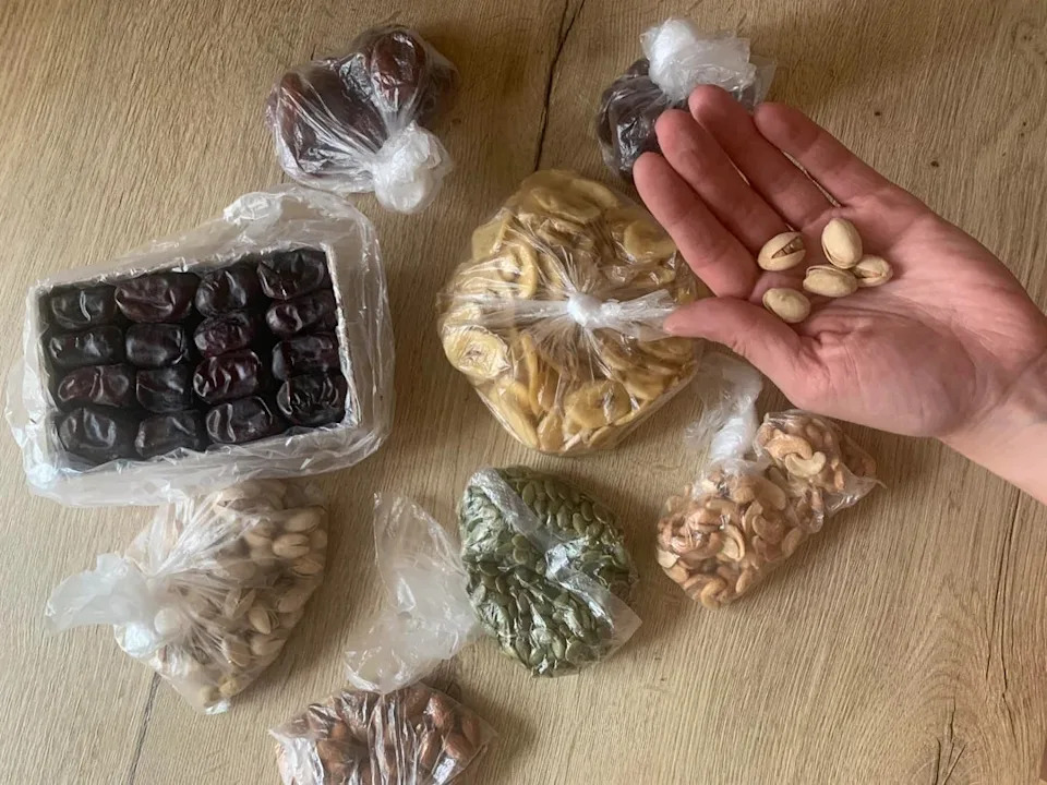 Assorted nuts and dried fruits in a bag on the table, hand holding pistachios