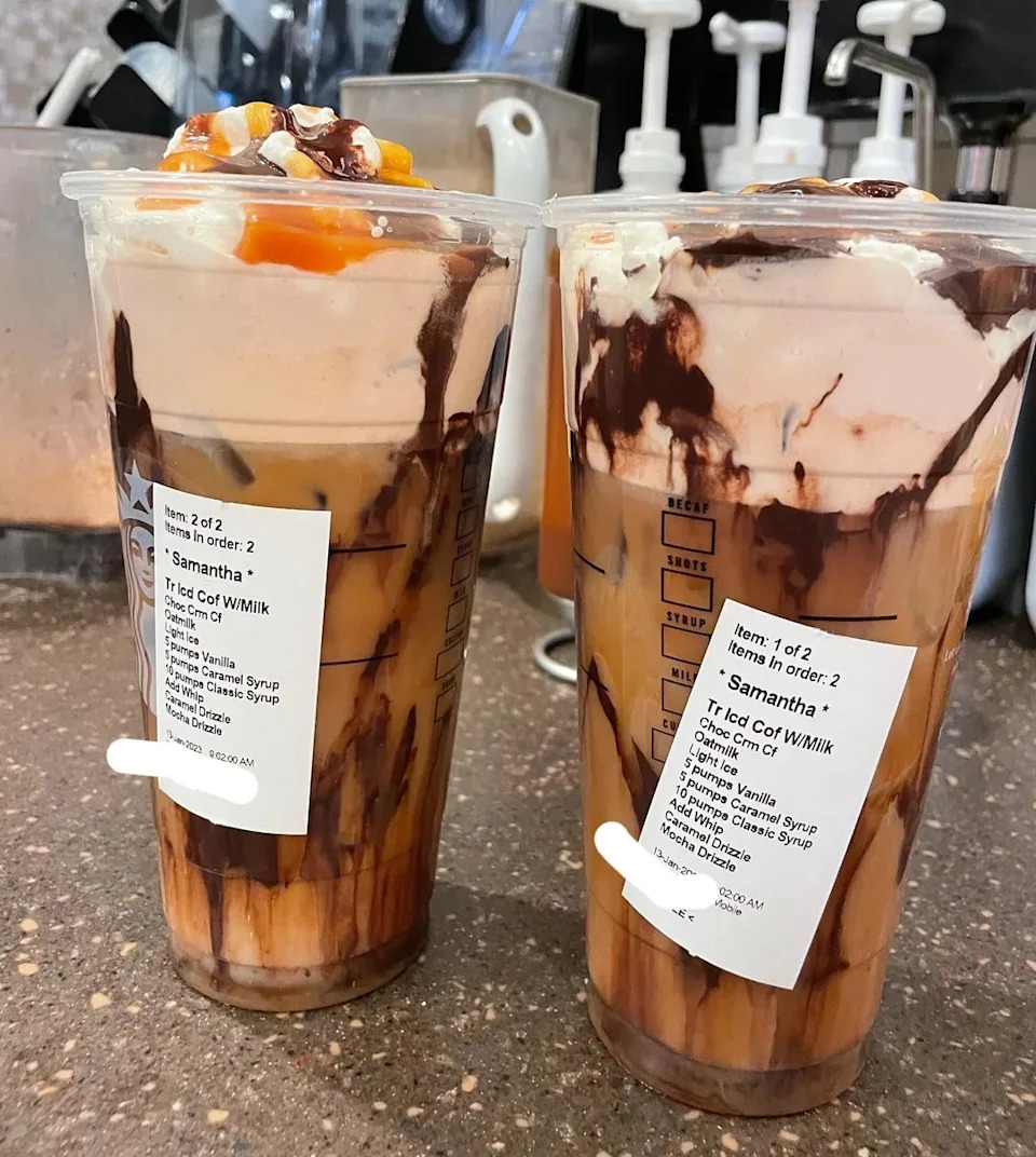Two iced coffee drinks topped with whipped cream, caramel drizzle, and chocolate syrup. The cup includes customization details.