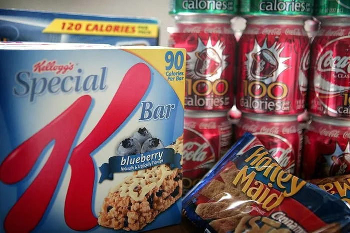 Special K Blueberry bars, Coke cans and Honey Maid graham crackers are shown, with the calorie content highlighted on the packaging.