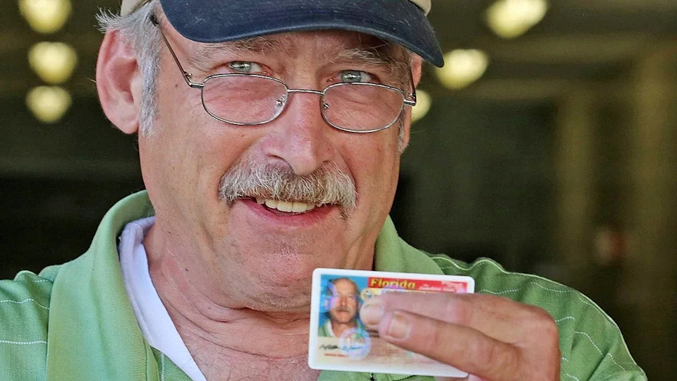 Benjamin Kyle places his finger over his real name on his Florida ID card.