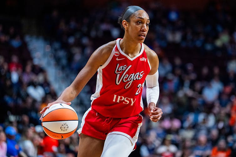 A young black woman in a red jersey dribbles a basketball.