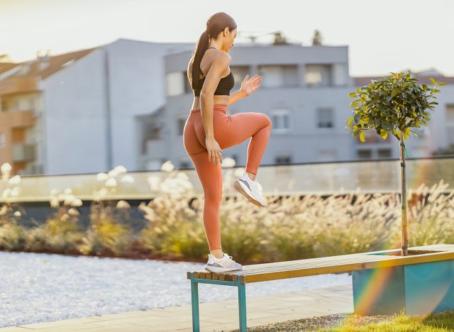 Healthy sportswoman is doing step-ups on a bench outdoors in the city.