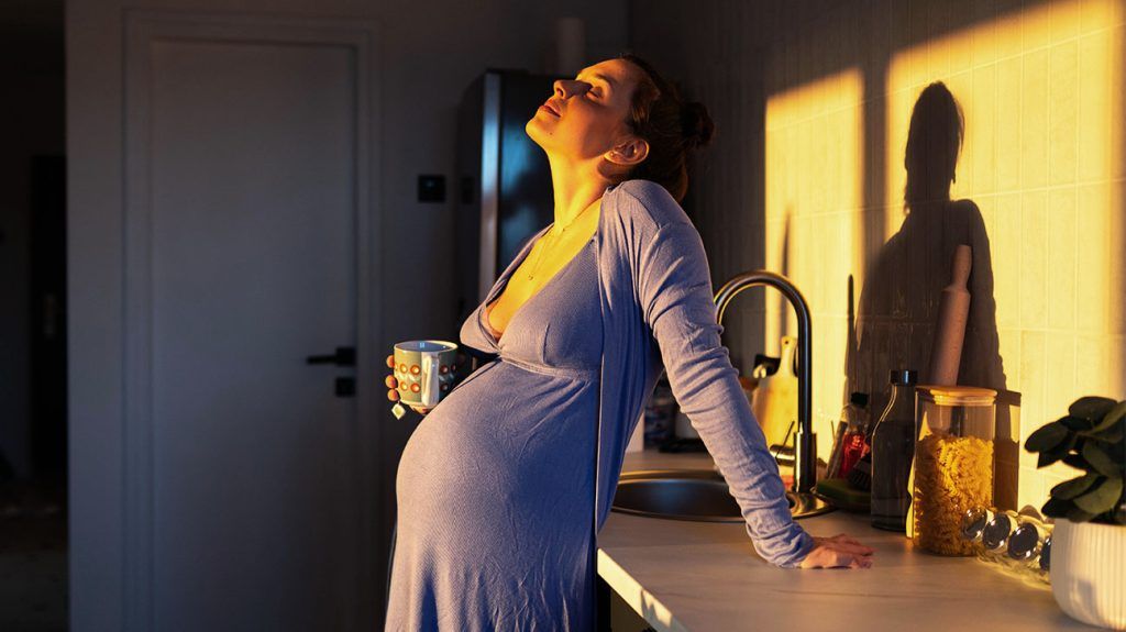 Young pregnant woman holding a mug in the kitchen